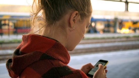 ung kvinde, bruge, en, Smartphone, hos, en, Tog Station, hos, en, slørede baggrund